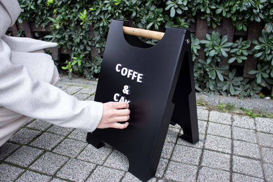 Person adjusting letters on a black outdoor sandwich sign for a café