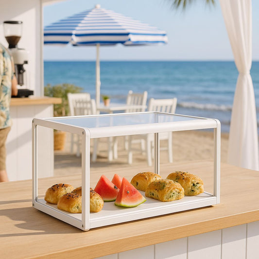 White display case with pastries and watermelon on a table by the beach.