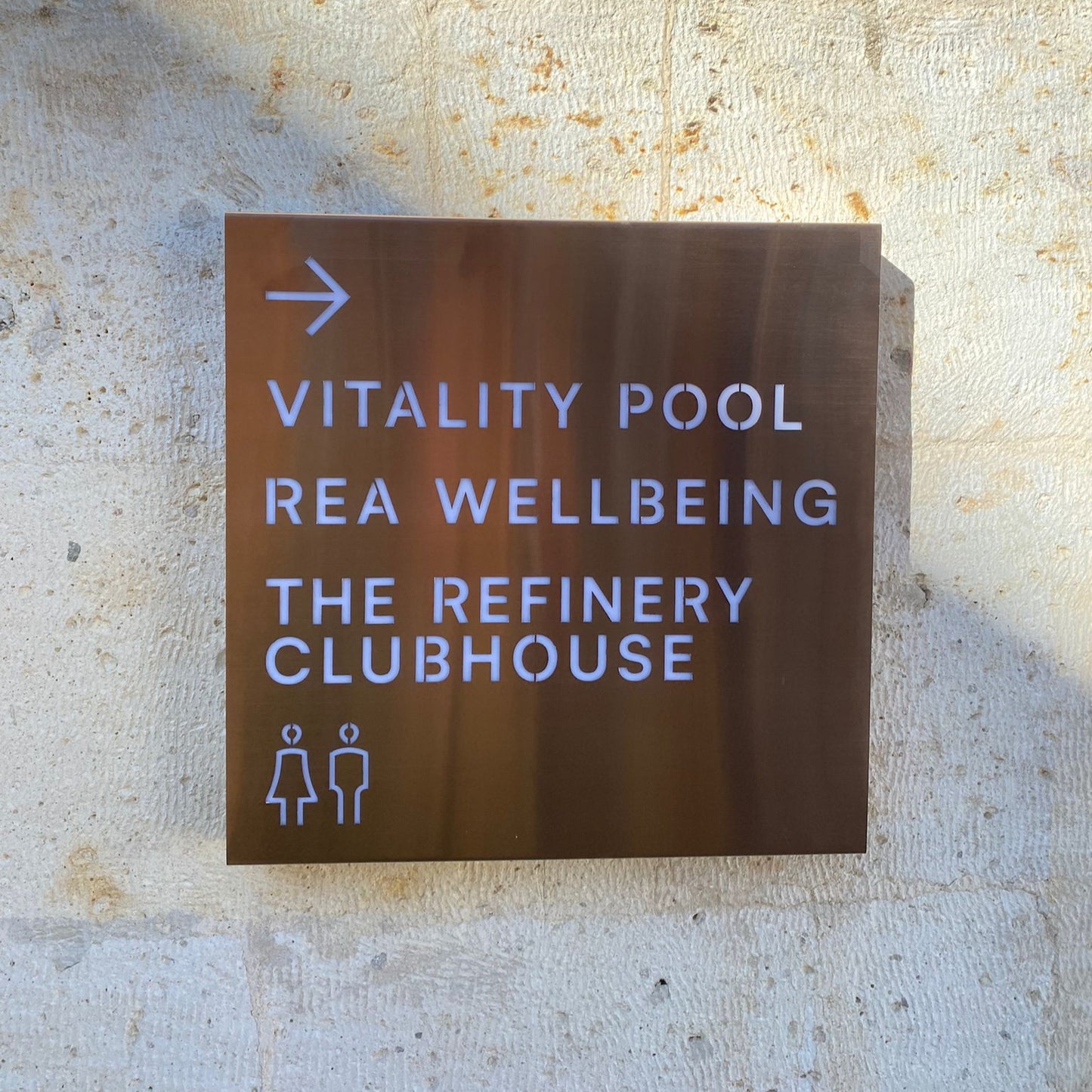 Directional sign pointing to Vitality Pool, REA Wellbeing, and The Refinery Clubhouse on a textured wall.
