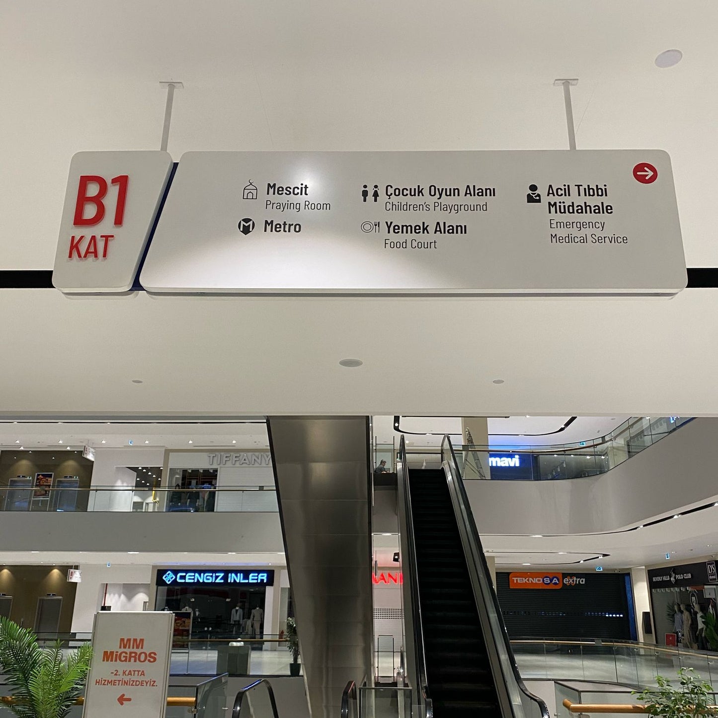 Mall interior with escalator and directional signs indicating different levels and facilities.