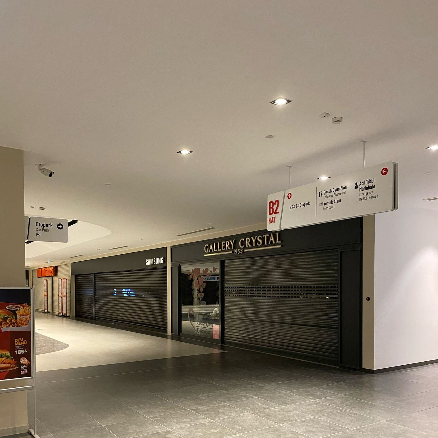 Empty shopping mall with closed storefronts and signs on the wall.