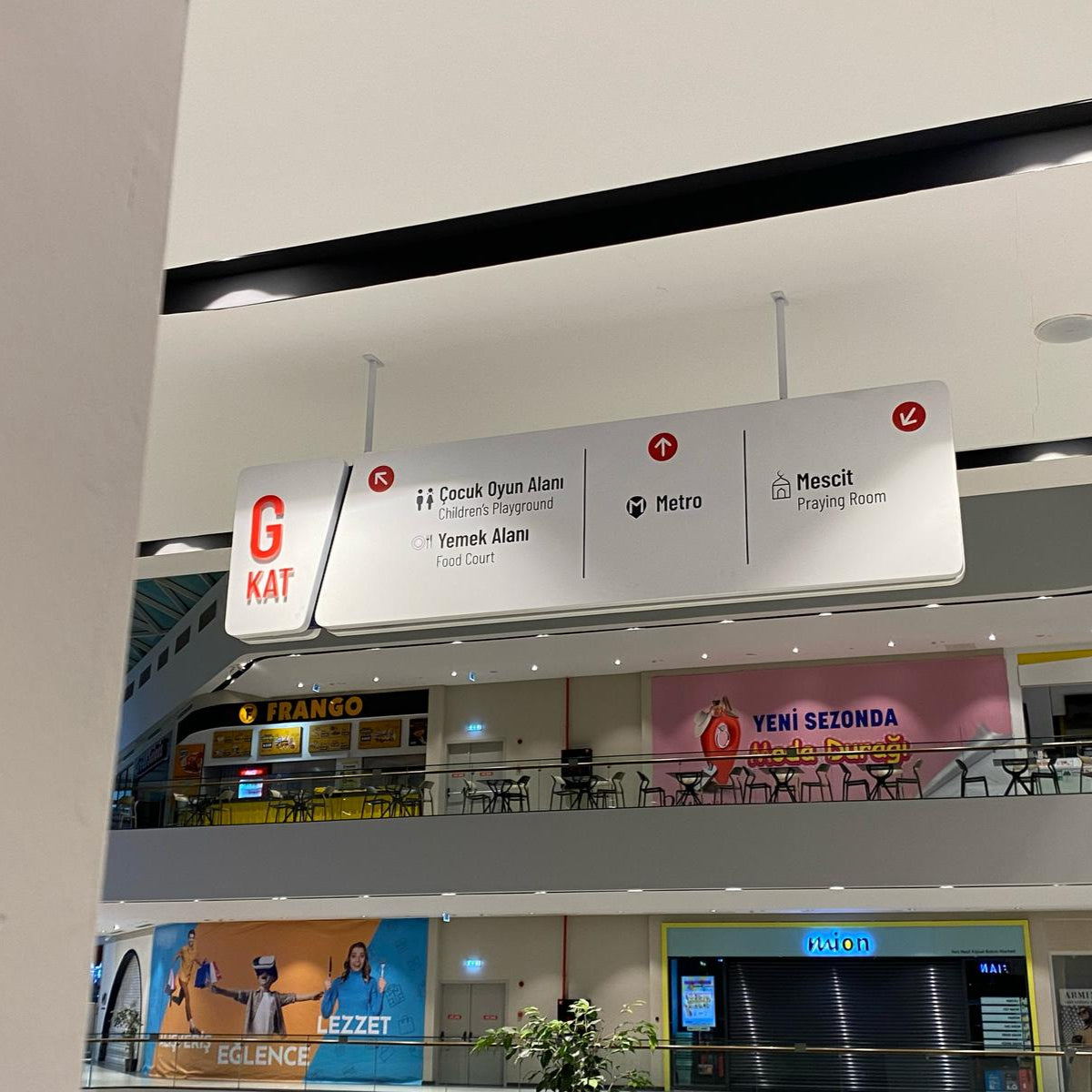 Signage in a shopping mall with various brands and directions.
