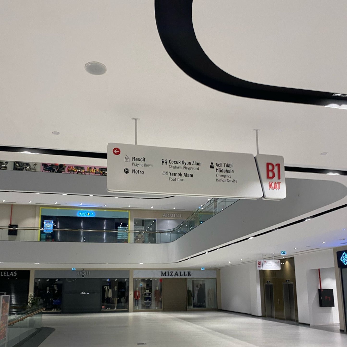 Modern indoor mall with a sign indicating B1 floor and various shops.