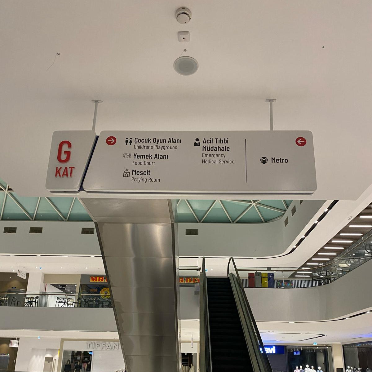 Escalator in a modern building with a directional sign above it.