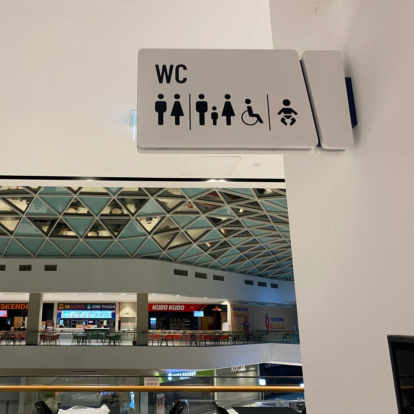 WC sign in an indoor setting with a modern architectural ceiling.