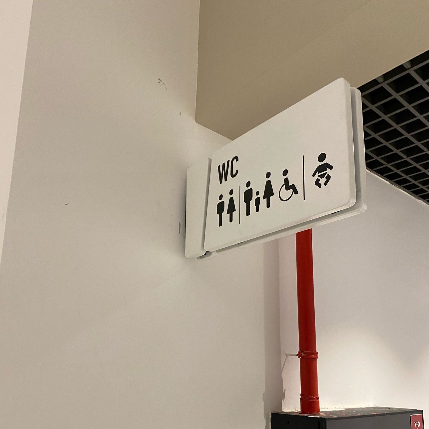 WC sign with accessibility icons on a wall next to a red pipe.