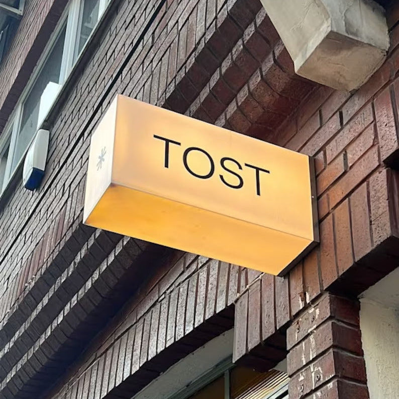 Gold sign with 'TOST' on a brick building