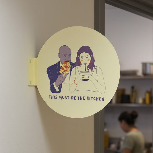 Round sticker with illustration of a couple and text 'This must be the kitchen' on a door, with a blurred kitchen background.