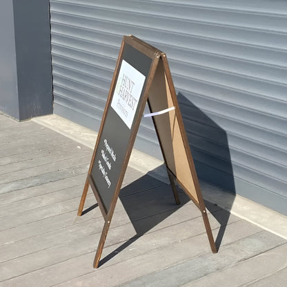 A-frame sign with a white poster on a wooden floor against a gray wall
