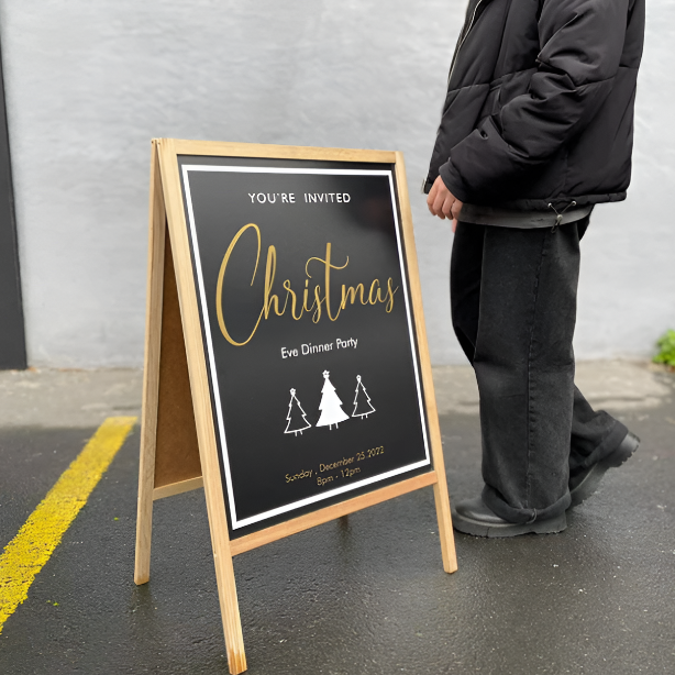 Person standing next to a Christmas party invitation sign on a street.