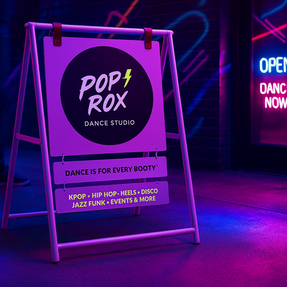Purple a-frame sign for Pop Rox Dance Studio with neon lights in the background