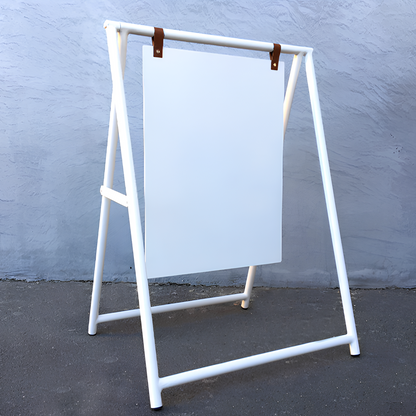 White a-frame sign stand with a blank white board against a gray wall.