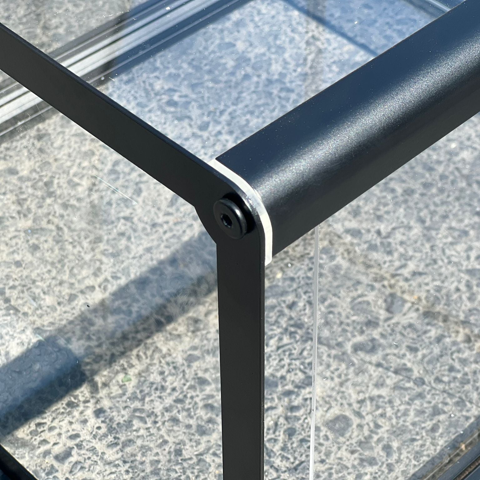 Close-up of a metal railing with glass panels on a textured surface