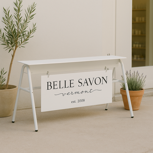 White stand with a 'Belle Savon Vermont' sign between two potted plants.