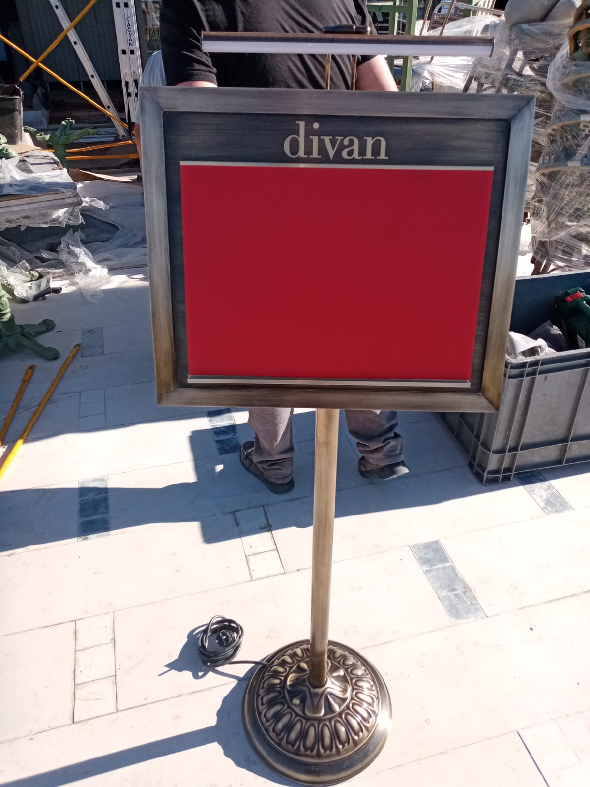 Red sign on a stand with 'divan' text, outdoors.
