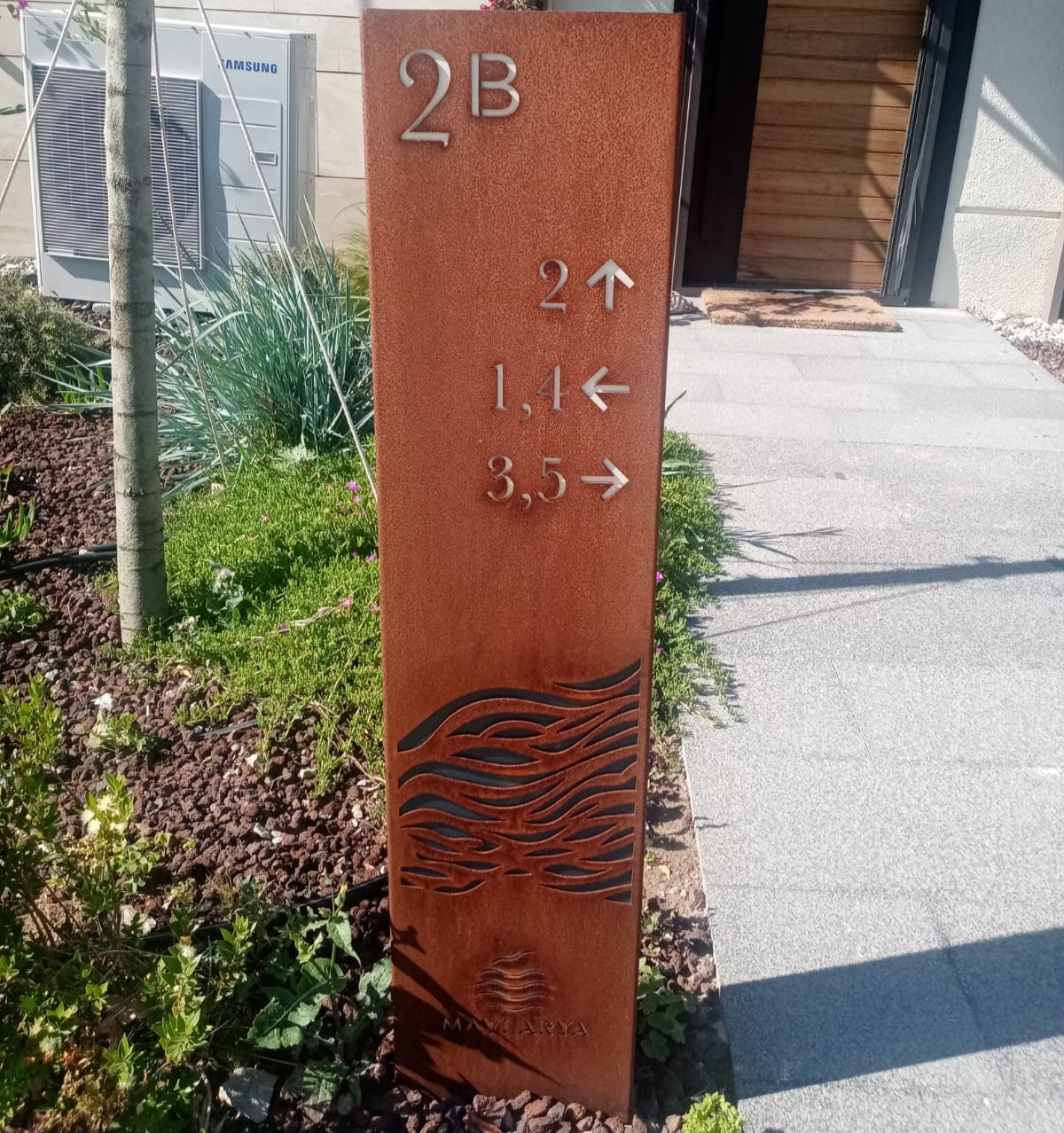 Metal sign with directional arrows and numbers on a sidewalk next to a building.