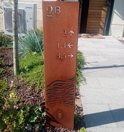 Metal sign with directional arrows and numbers on a sidewalk next to a building.