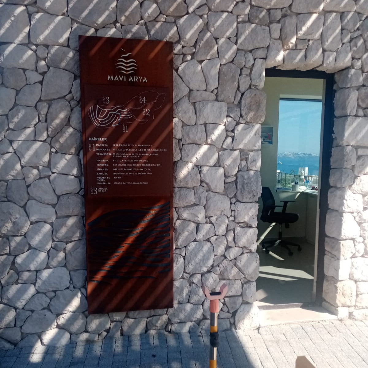 Signboard with text and symbols on a stone wall, with a person holding a broom in the foreground.