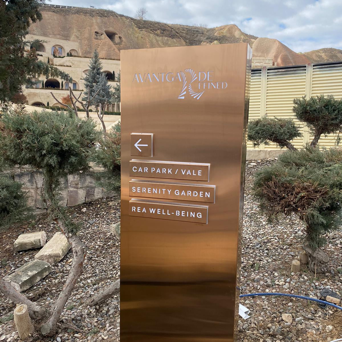 Bronze directional sign in a garden setting with mountains in the background