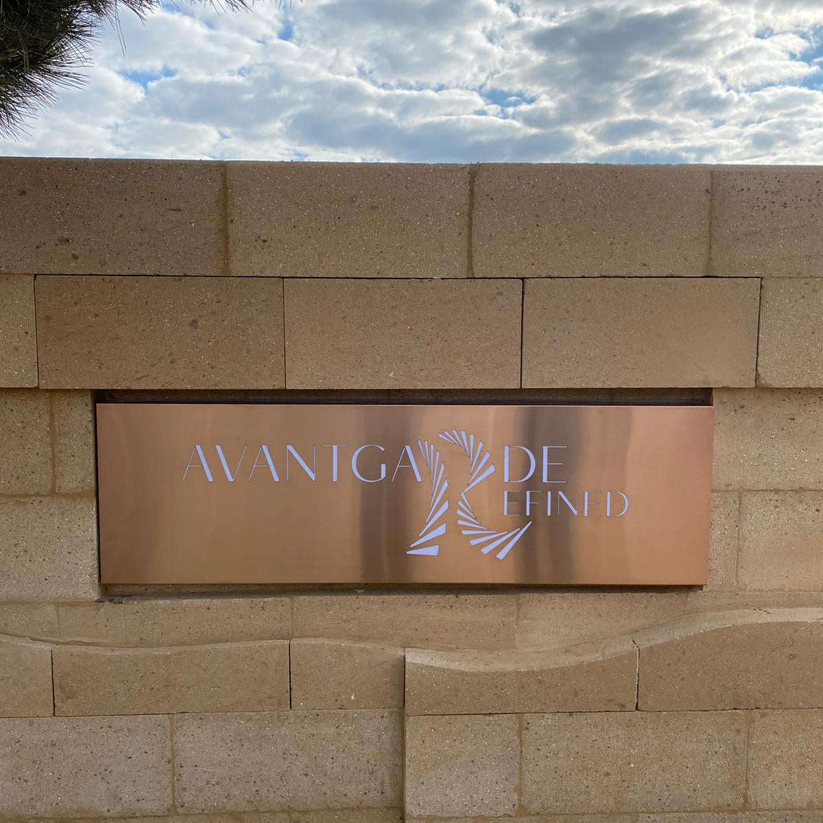 Brass sign with 'Avangarde' on a stone wall against a cloudy sky