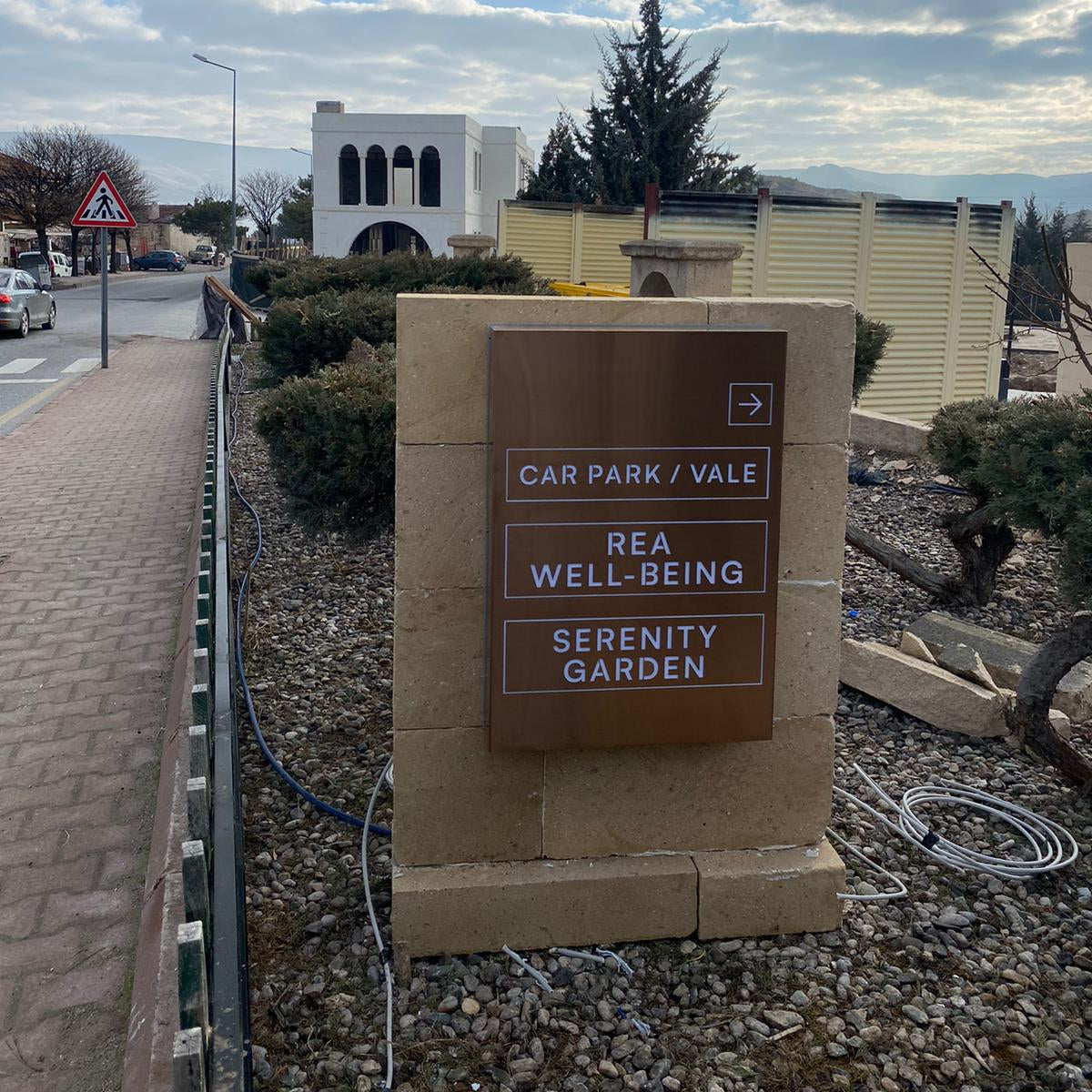 Sign pointing to 'Car Park Vale', 'REA Well-Being', and 'Serenity Garden' with a cloudy sky.