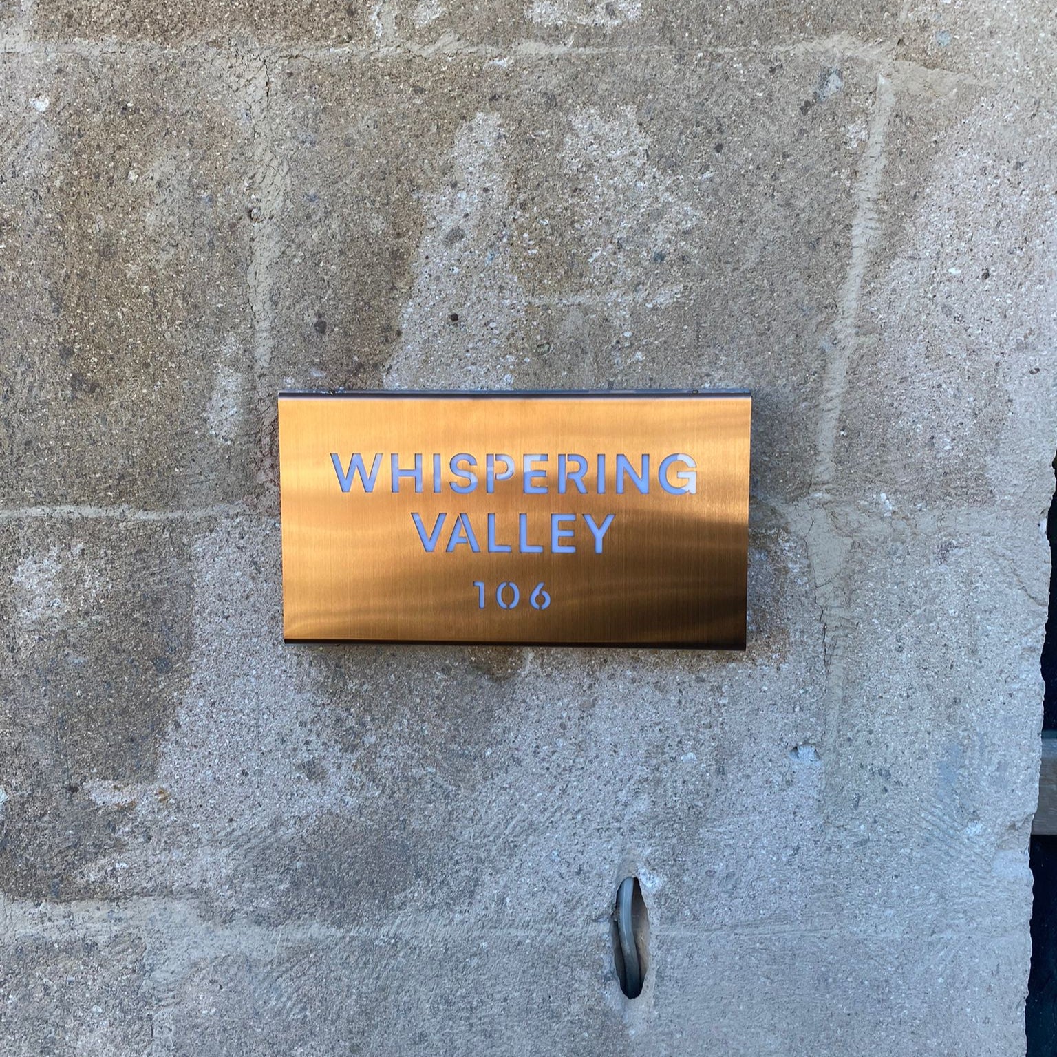 Brass plaque with 'Whispering Valley 106' on a stone wall
