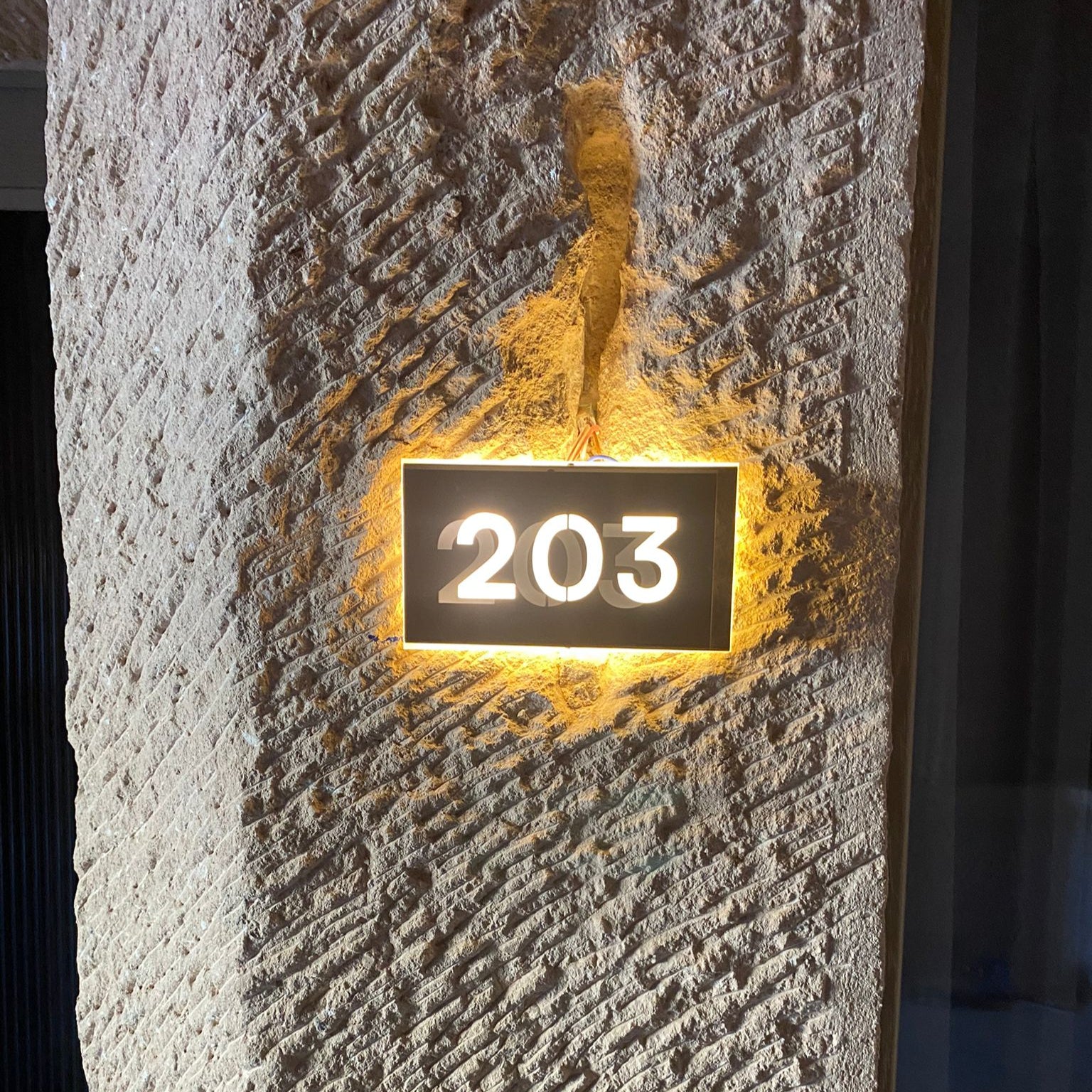 Lighted house number sign '203' on a textured stone wall.