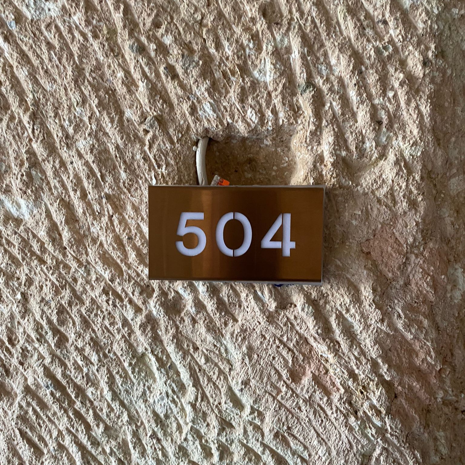 Metal house number plate with '504' on a textured wall.