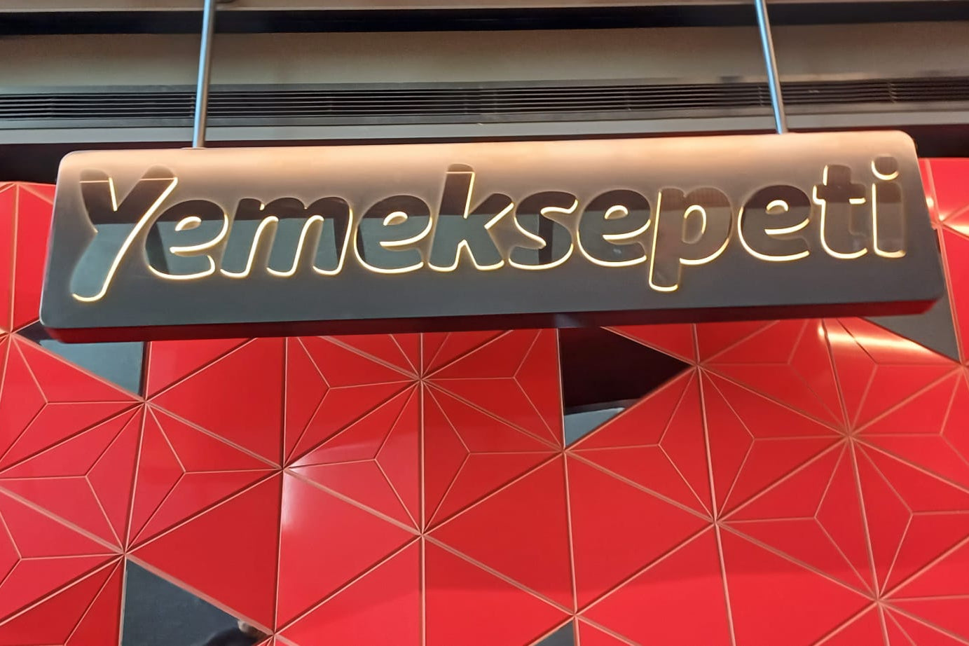 Yemeksepeti logo on a red geometric-patterned wall