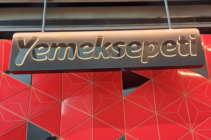 Yemeksepeti logo on a red geometric-patterned wall