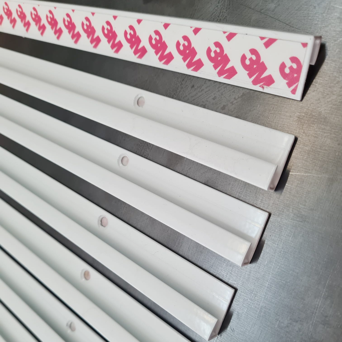 Back of white interchangeable menu board rails showing mounting holes and 3M adhesive strip