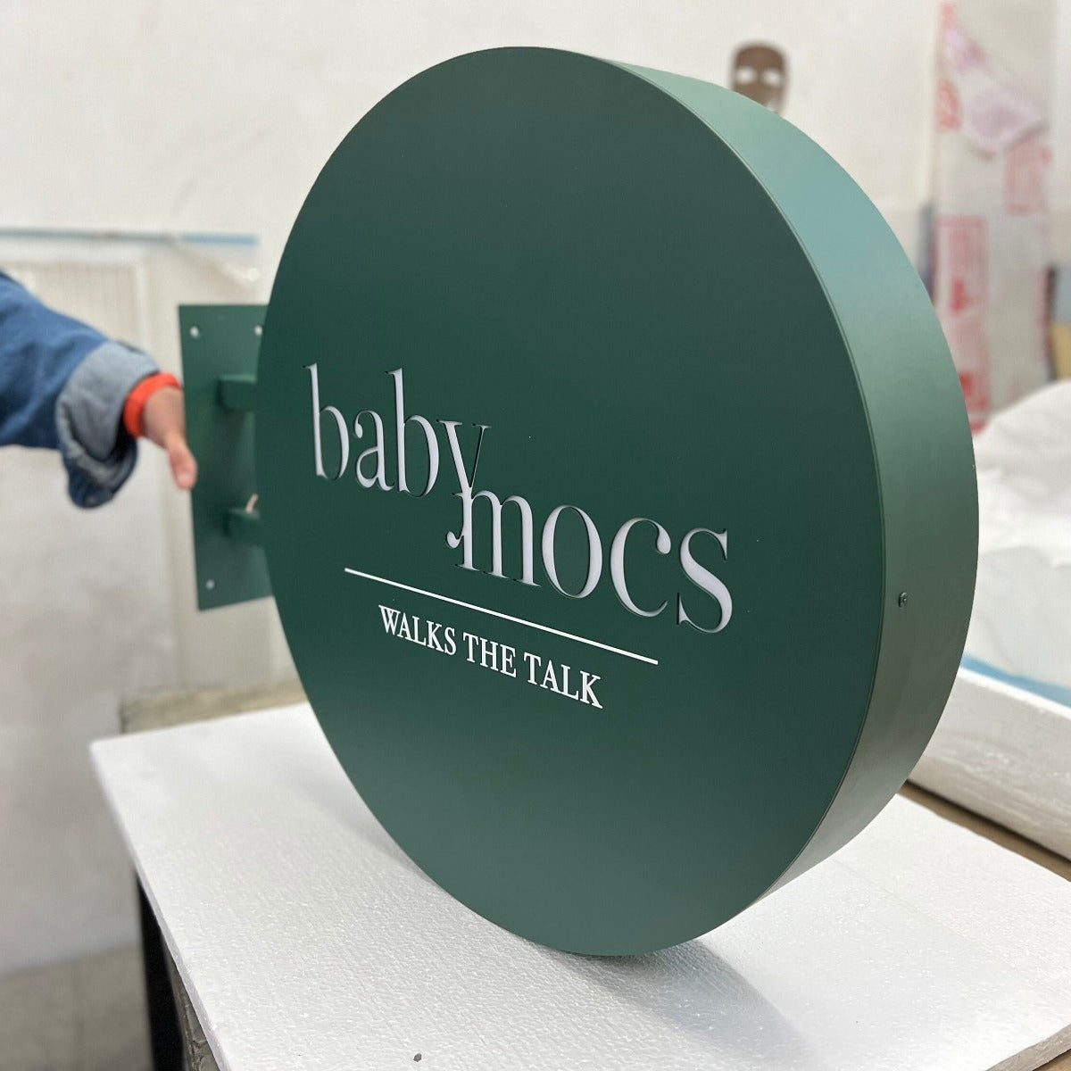 Round green sign with 'baby mocs' text on a white surface