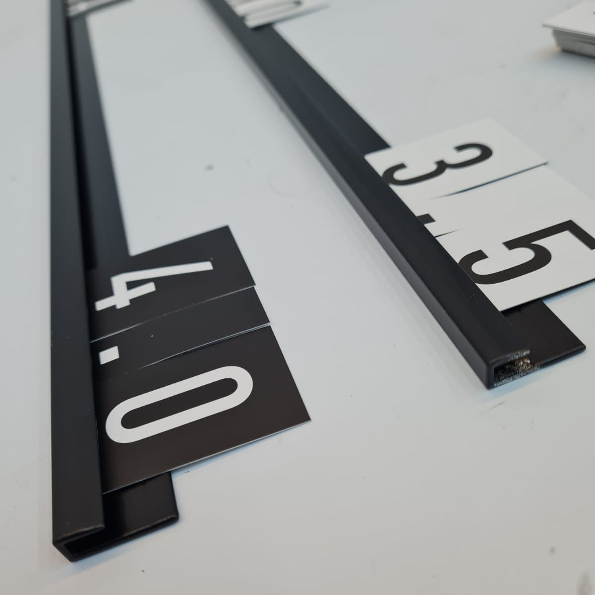 Close-up of a measuring tape with black frame and white measurement numbers on a light gray background.