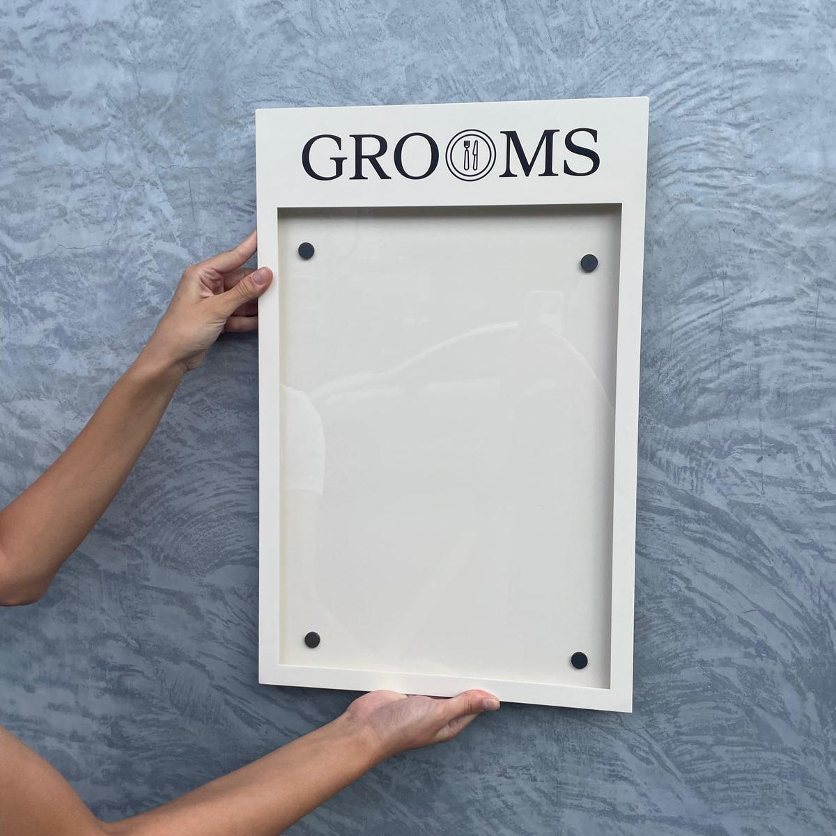 White picture frame with 'GROOMS' text held against a gray textured wall.