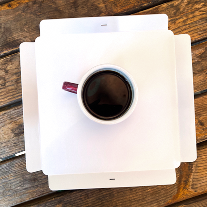 White mug with dark liquid on a white square coaster on a wooden surface