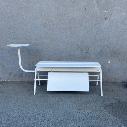 White metal desk with attached side table against a gray wall.