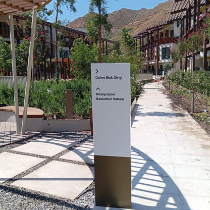 Tall white sign with text on a pathway in an outdoor setting