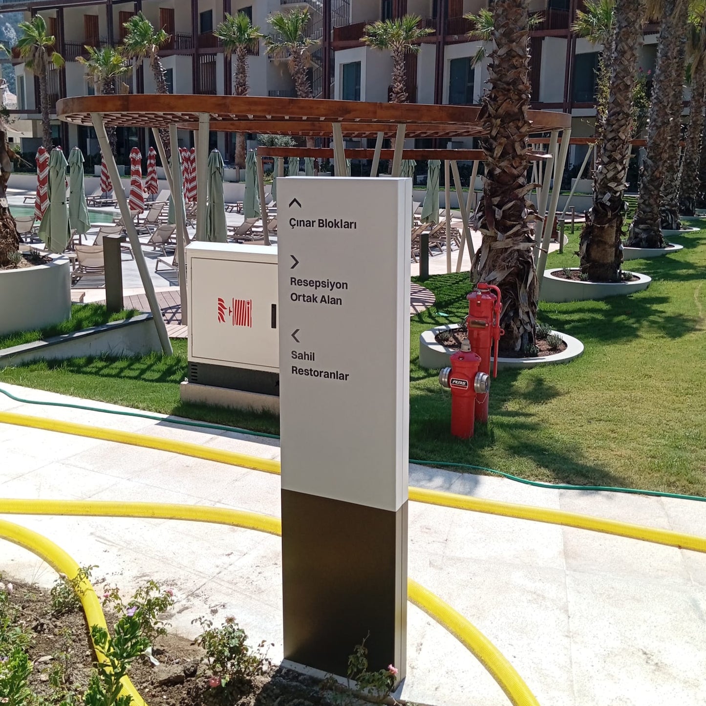 Outdoor setting with a signpost, palm trees, and a building in the background.