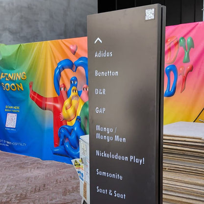 Directional sign with brand names on a wall next to colorful posters