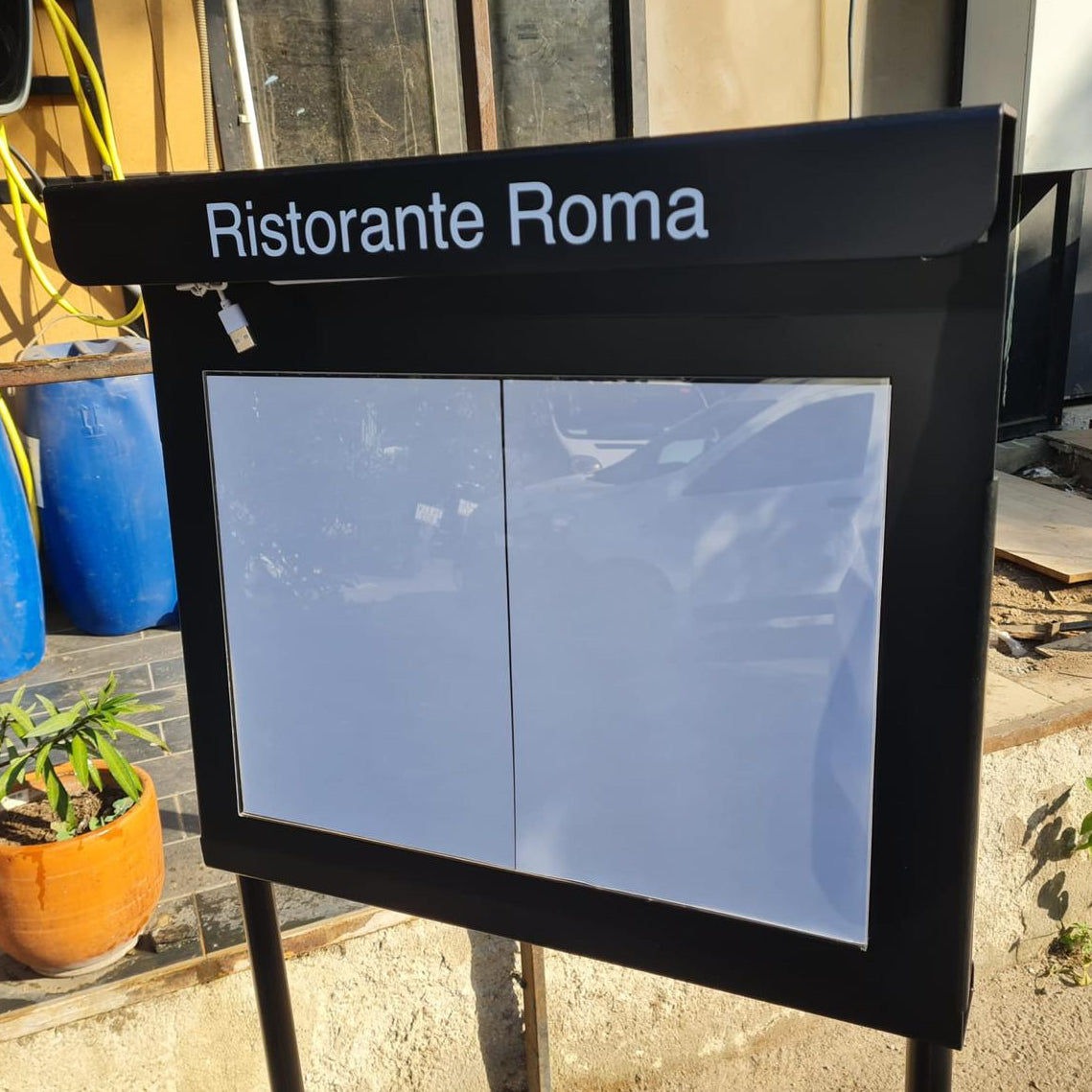 Outdoor sign for Ristorante Roma with potted plants and a building in the background