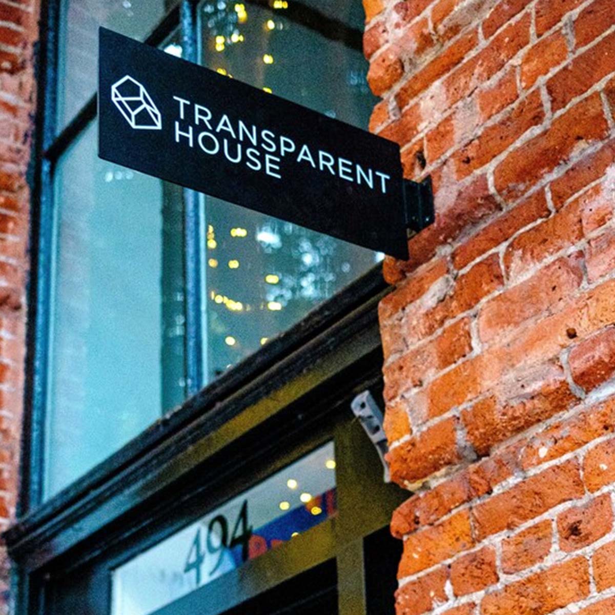 Transparent House sign on a brick building with blurred lights in the background
