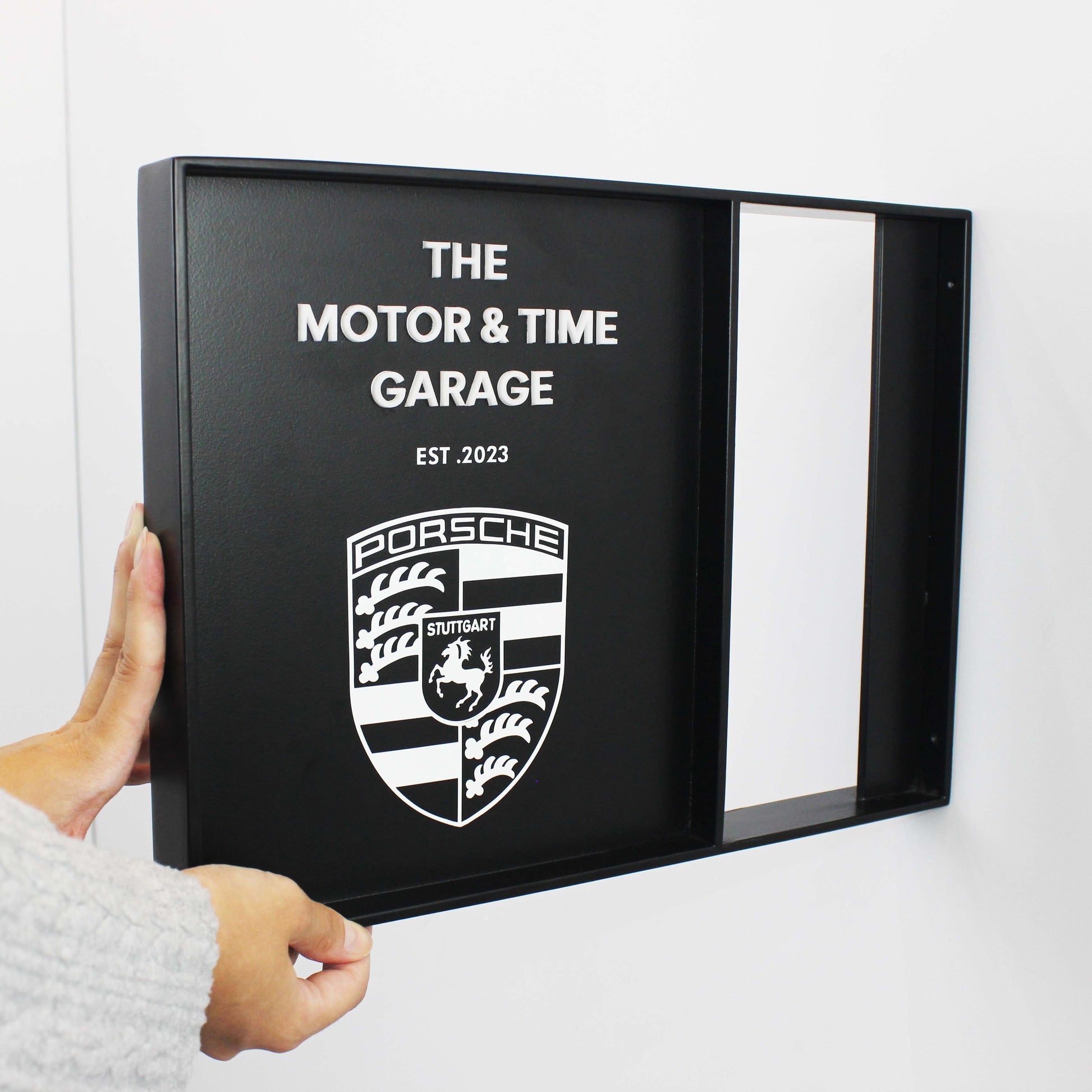 Person holding a black framed sign with Porsche logo and text on a white background