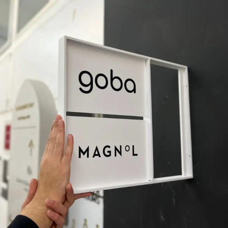 Hand touching a sign with 'goba' and 'MAGNOL' on a black background