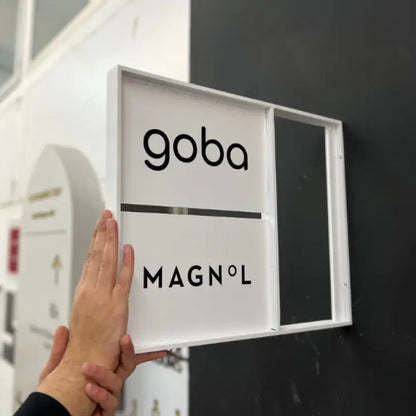 Hand touching a sign with 'goba' and 'MAGNOL' on a black background