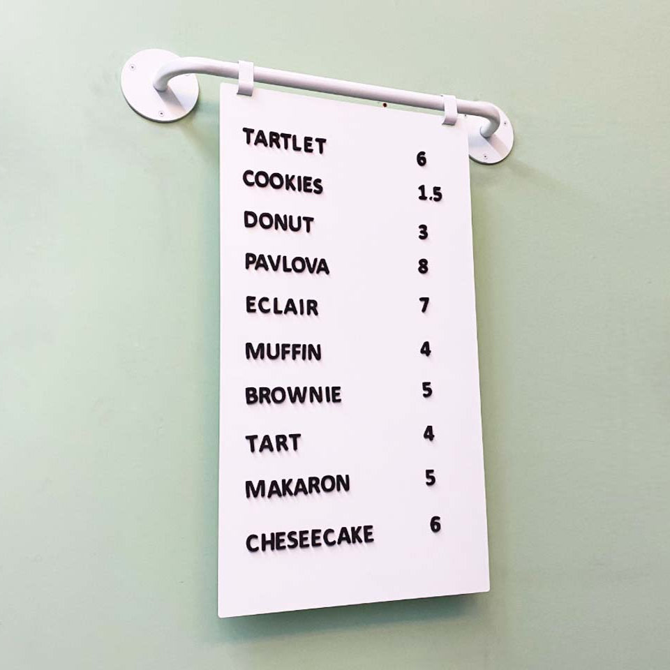 White towel with black text listing dessert names and quantities on a light green wall.