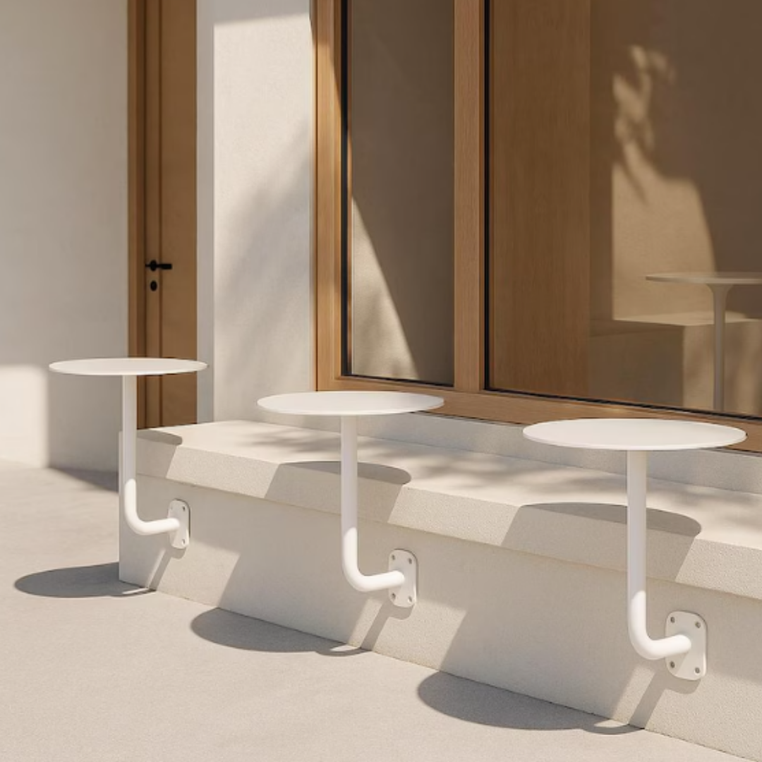 Modern outdoor seating area with white tables and benches against a neutral wall.