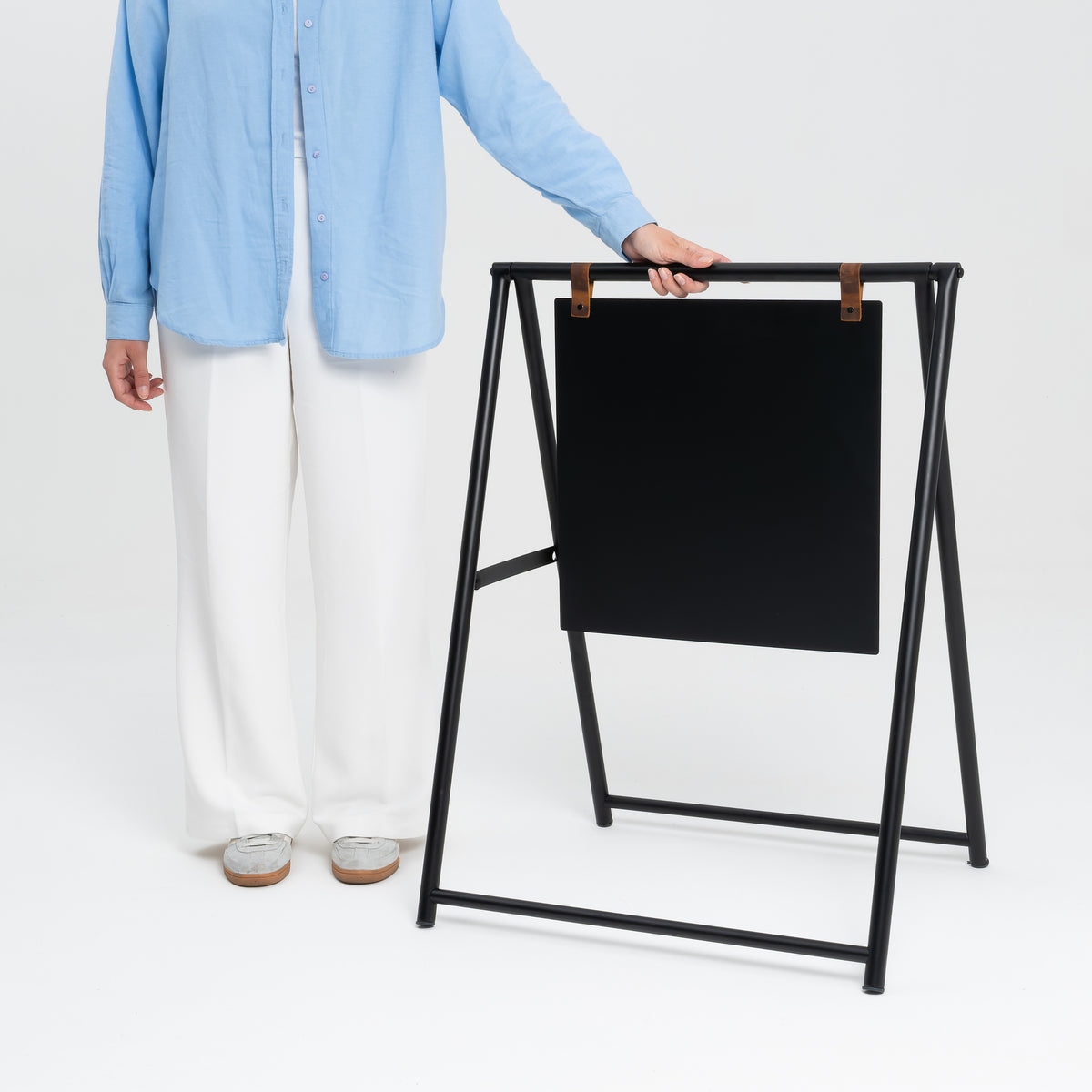 Person carrying an unprinted black A-frame sign for scale